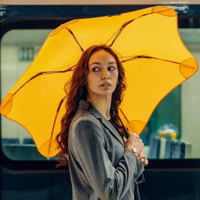 Woman holding a large yellow umbrella in an urban setting