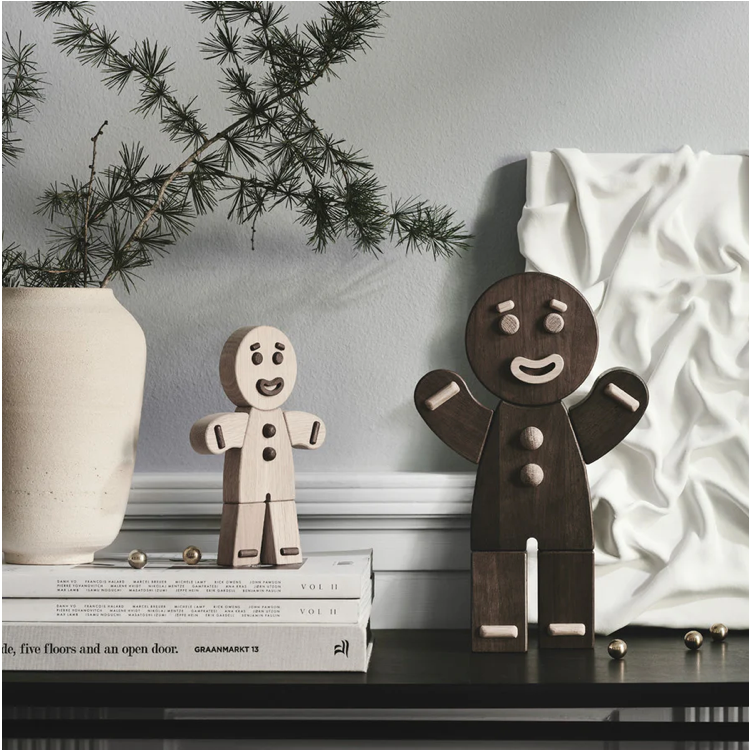 Two wooden gingerbread man figures on a shelf with a decorative plant and white vase in the background.