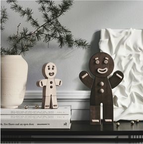 Two wooden gingerbread man figures on a shelf with a decorative plant and white vase in the background.