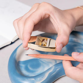 Hand using a gold-colored pencil sharpener on a blue ceramic surface