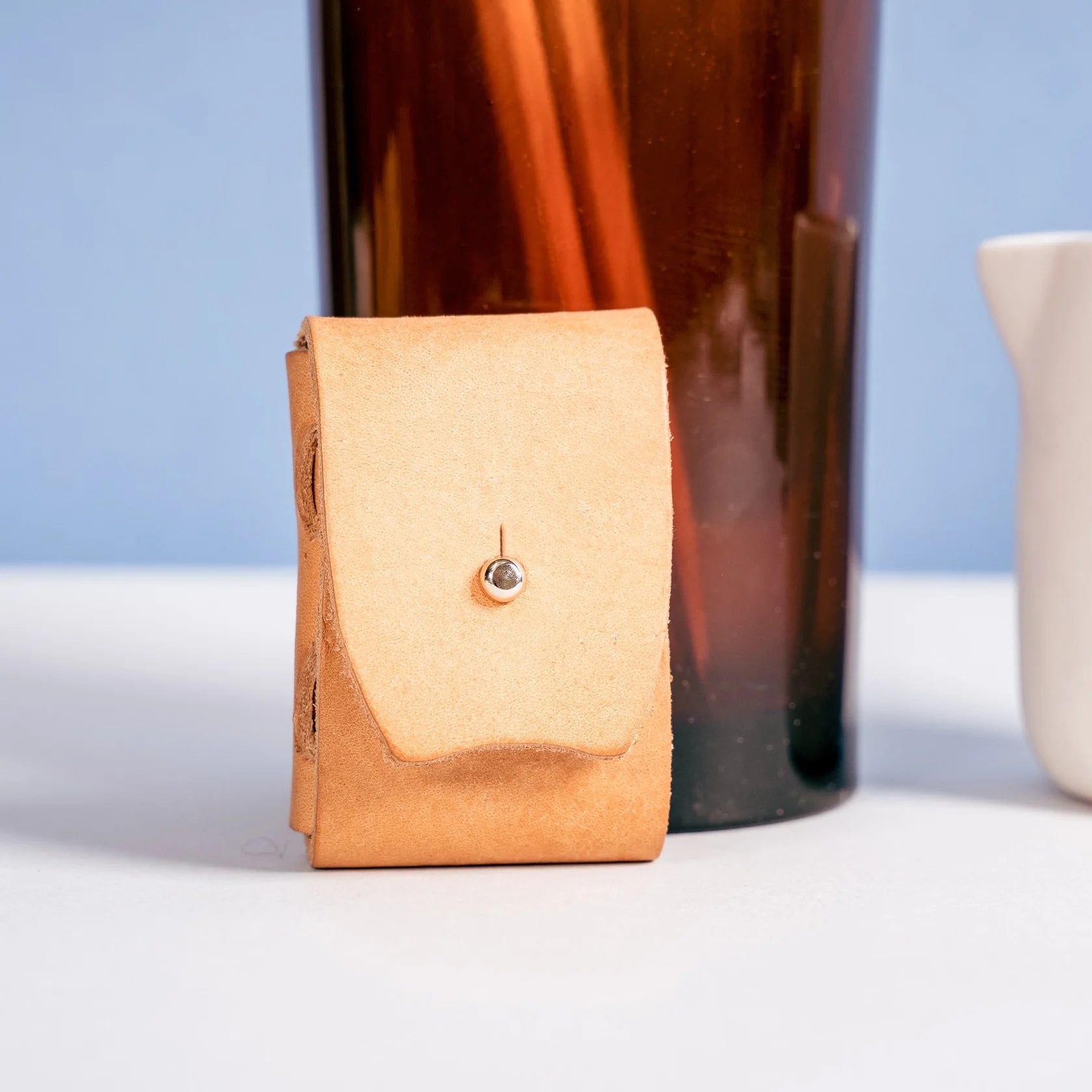 Tan leather pouch with a metallic clasp on a white surface with a blue background