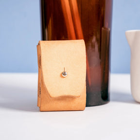 Tan leather pouch with a metallic clasp on a white surface with a blue background