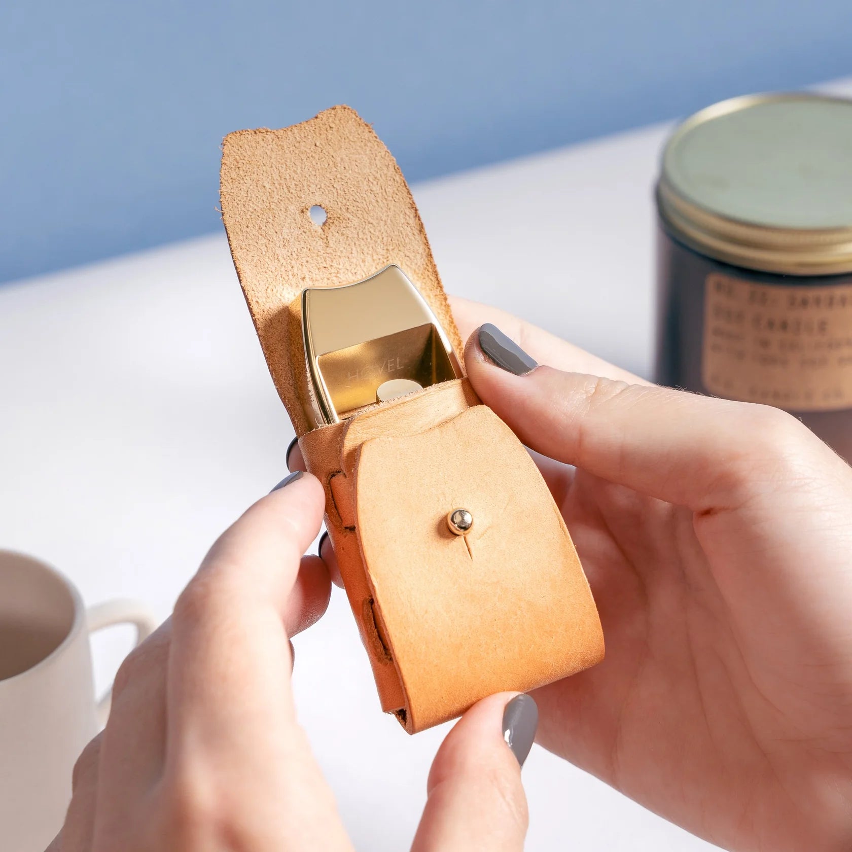 Person holding a small brown leather case with a gold clasp on a light surface.