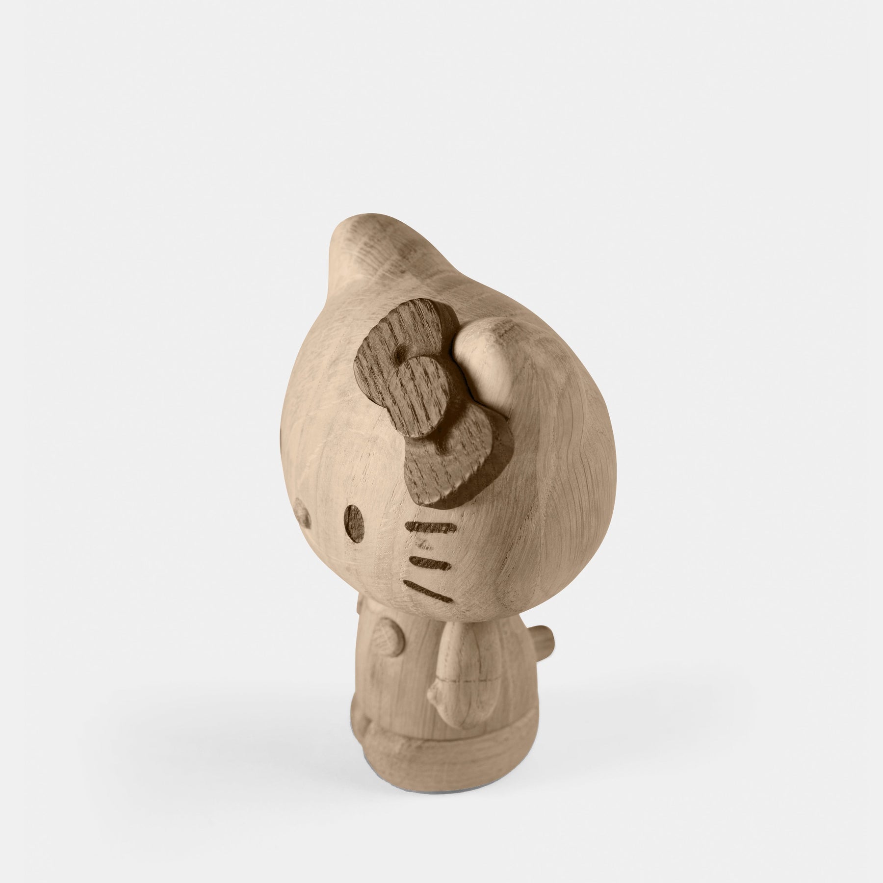 Wooden figurine of an animated cartoon character carved from light oak, featuring a rounded head with a carved bow detail, minimal facial markings, a smooth sculpted body with small arms, visible natural wood grain, and a matte surface on a plain white background.