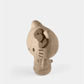 Wooden figurine of an animated cartoon character carved from light oak, featuring a rounded head with a carved bow detail, minimal facial markings, a smooth sculpted body with small arms, visible natural wood grain, and a matte surface on a plain white background.