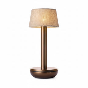 A modern table lamp with a textured beige fabric drum shade, a brushed bronze metal stem, and a matching round bronze base, shown against a solid white background.