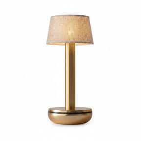 A modern table lamp with a brushed brass-finished metal base and stem, featuring a textured beige fabric drum shade, shown against a solid white background.
