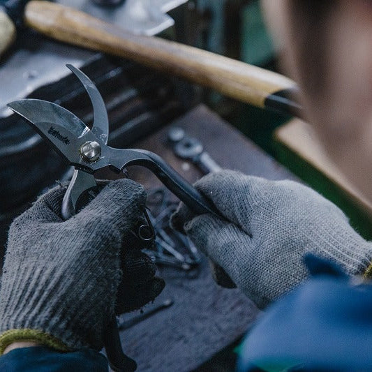 Person wearing gloves holding a pair of shears over a workbench with tools in the background