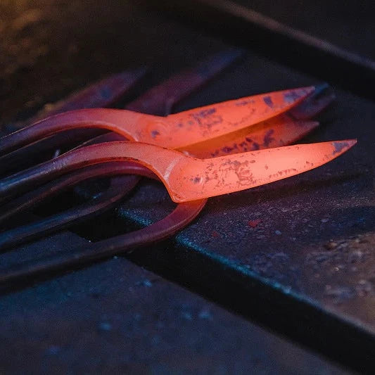 A close-up of glowing hot metal tools or bars resting on a dark workbench, with one piece illuminated in bright orange-red heat.