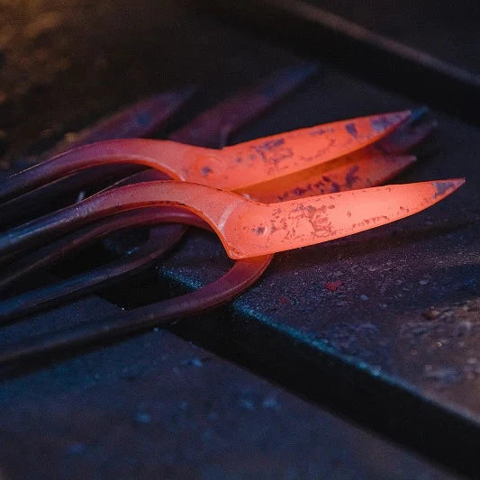 A close-up of glowing hot metal tools or bars resting on a dark workbench, with one piece illuminated in bright orange-red heat.