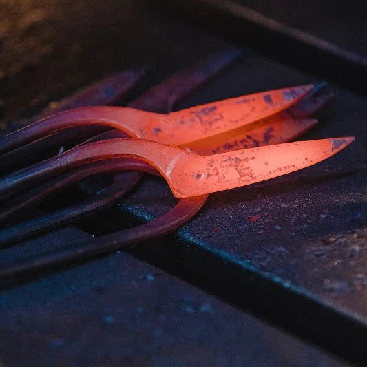 A close-up of glowing hot metal tools or bars resting on a dark workbench, with one piece illuminated in bright orange-red heat.