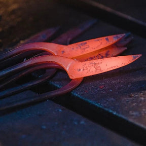 A close-up of glowing hot metal tools or bars resting on a dark workbench, with one piece illuminated in bright orange-red heat.