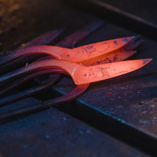 A close-up of glowing hot metal tools or bars resting on a dark workbench, with one piece illuminated in bright orange-red heat.