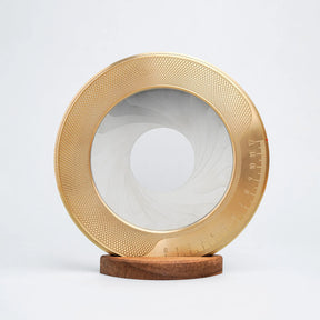 Decorative plate with gold rim and white center on a wooden stand against a light gray background