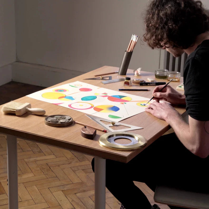Person painting a color wheel on paper with art supplies on a table.