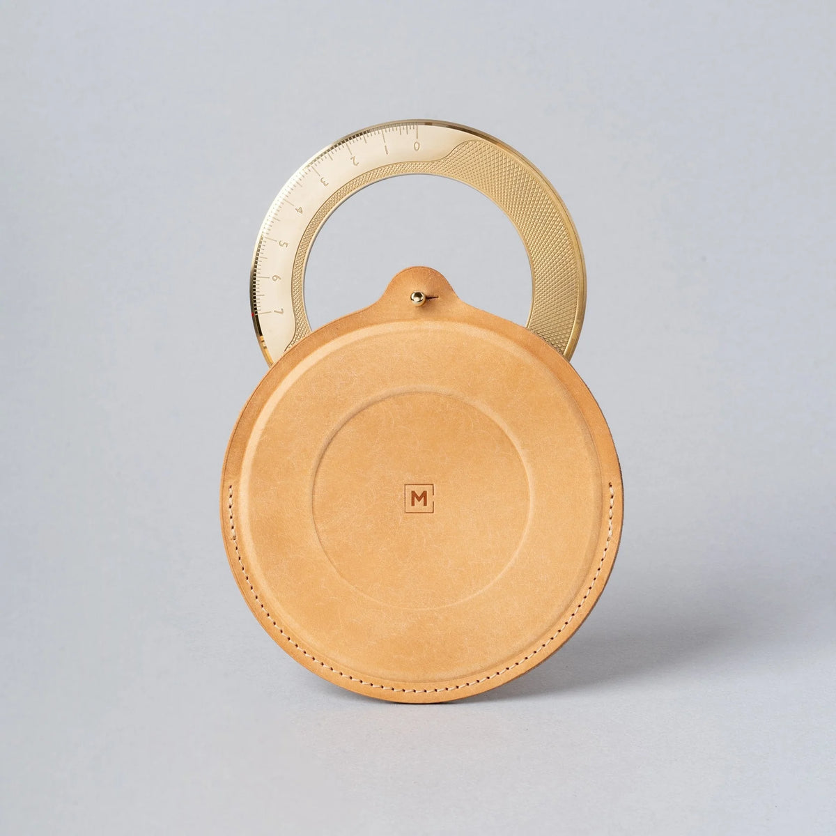 Round tan leather product with gold handle on a light gray background