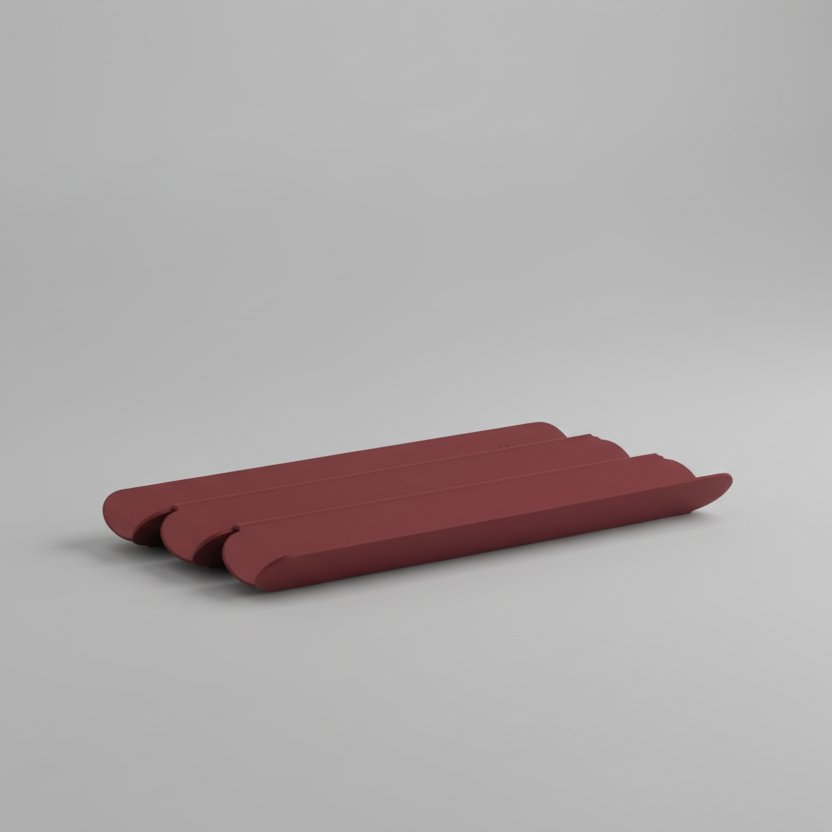 Burgundy Karst pen tray with rounded edges and layered ridges, photographed at an angle on a soft gray background to highlight its minimalist, low-profile design.