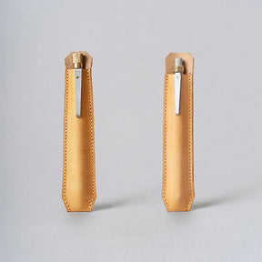 Two tan leather pen holders with metal clips on a gray background