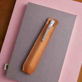 Brown leather knife sheath on a gray notebook with a pink background
