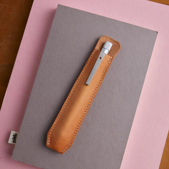 Brown leather knife sheath on a gray notebook with a pink background