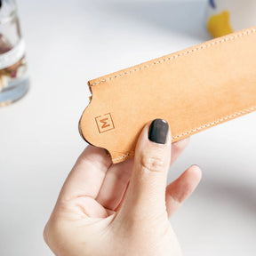 Hand holding a tan leather wallet with a brand logo on a light background