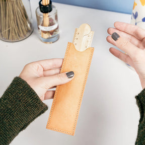Person holding a leather pencil case with a ruler on a light surface