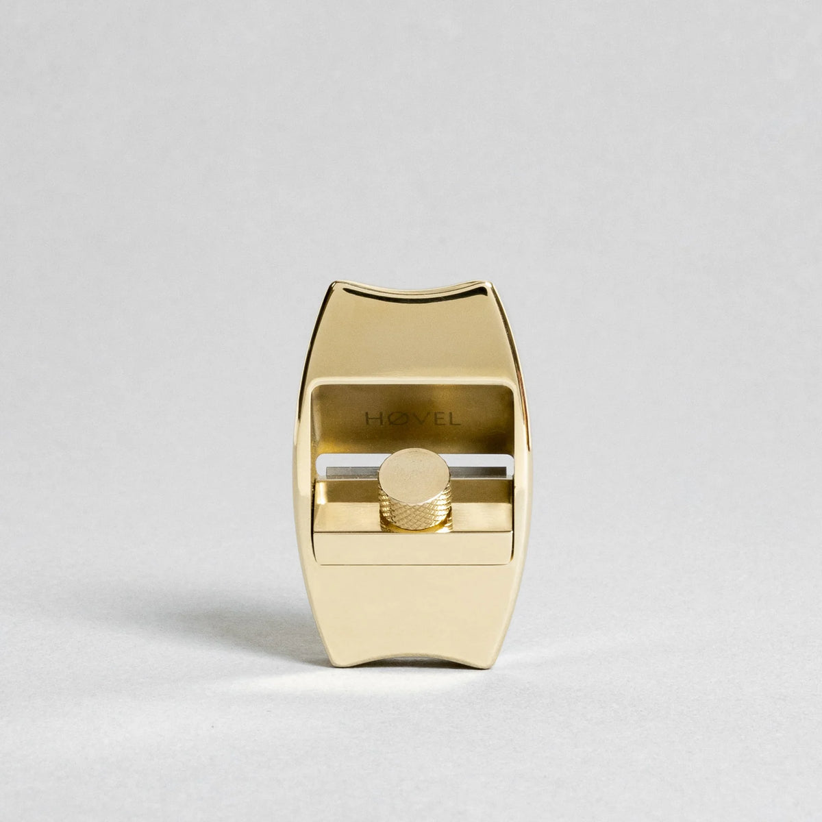 Front view of a polished brass Høvel pencil sharpener with a knurled adjustment knob, centered against a light gray background.