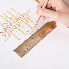 Hand holding a pen with gold calligraphy and a ruler on a white background