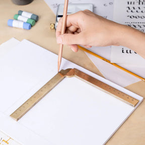 Hand holding a pencil with a protractor on a desk with stationery items.