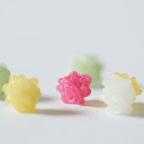 Five small, textured, flower-like beads in pastel colors including light green, yellow, pink, white, and pale yellow, arranged on a plain white surface with a shallow depth of field.