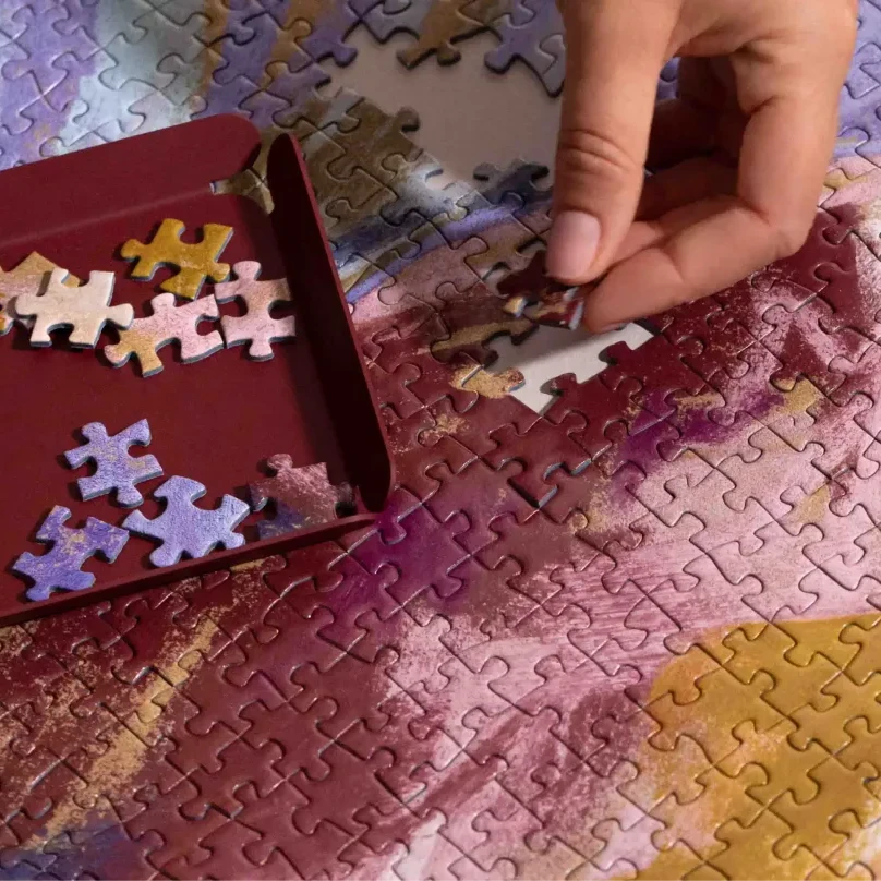 Person assembling a puzzle with a colorful design on a table.