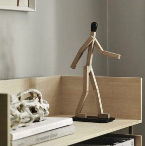 Wooden sculpture of a walking figure on a shelf with books and decorative items.