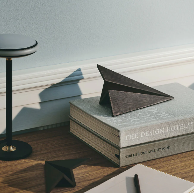 Stack of books titled 'The Design Hotels' with a geometric wooden object on top, placed on a wooden surface.