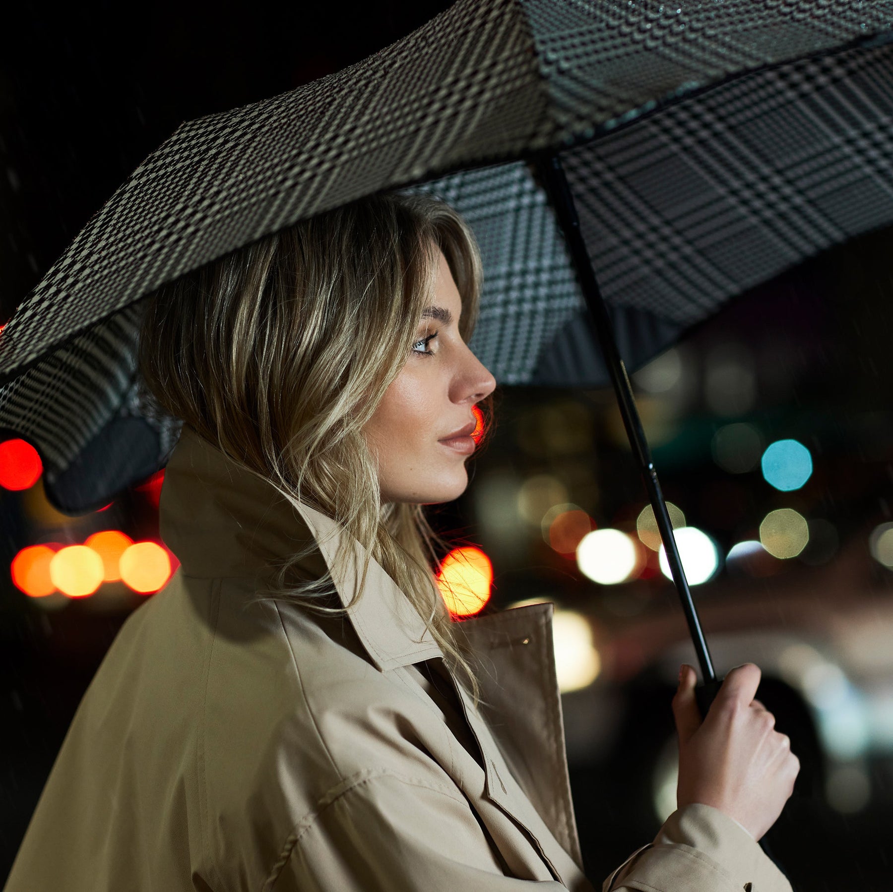 Woman holding an umbrella in a city street at night with blurred lights in the background