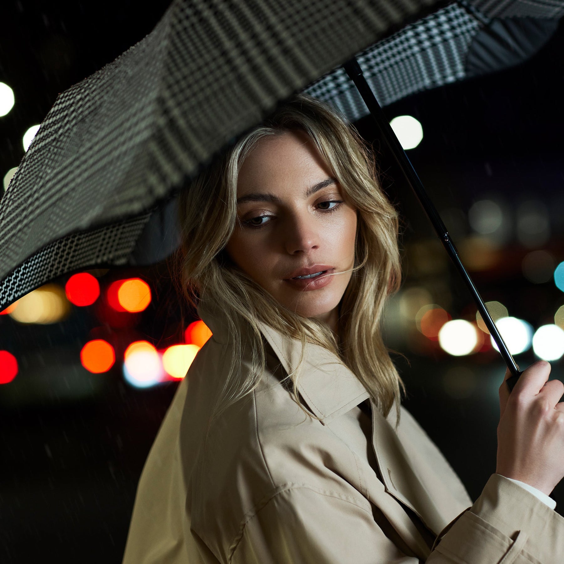 Woman holding an umbrella against a night cityscape with blurred lights