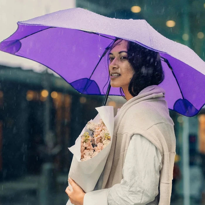 Woman holding a purple umbrella and a bouquet of flowers in the rain.