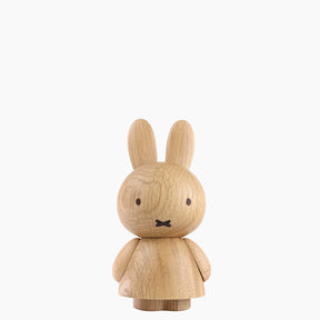 Front view of a wooden figurine of an animated cartoon character carved from light oak, featuring long upright ears, simple facial details, a rounded sculpted body with small arms, visible natural wood grain, and a matte surface on a plain white background.