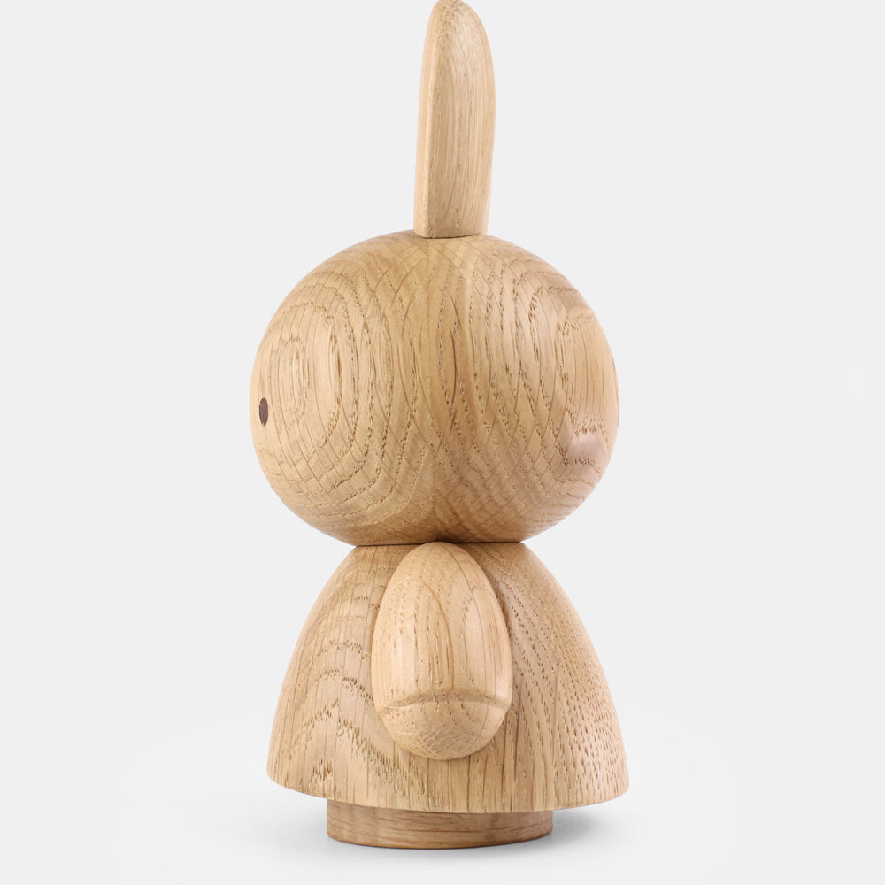Wooden figurine of an animated cartoon character carved from light oak, featuring a rounded head with one long upright ear visible, minimal facial detail, a smooth sculpted body with small arms, visible natural wood grain, and a matte surface on a plain white background.
