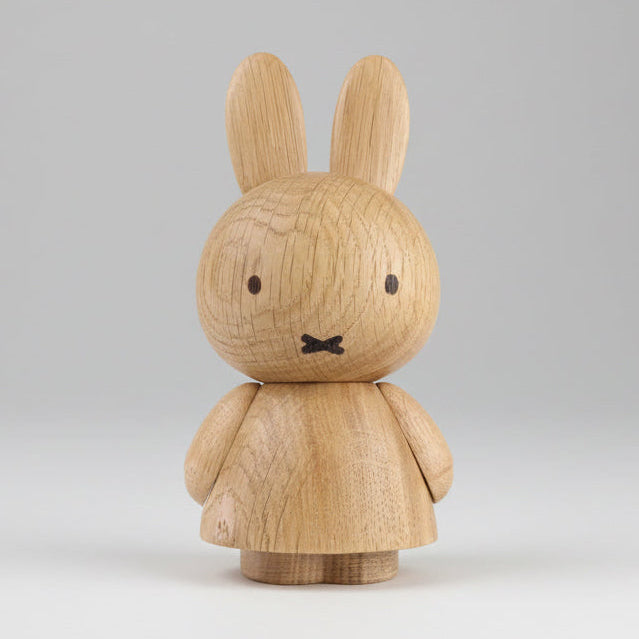 Front view of a wooden figurine of an animated cartoon character carved from light oak, featuring long upright ears, simple facial details, a rounded sculpted body with small arms, visible natural wood grain, and a matte surface on a plain white background.