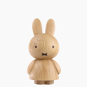 Wooden figurine of an animated cartoon character carved from light oak, featuring long upright ears, simple dot eyes and crossed mouth detail, a rounded sculpted body with small arms, visible natural wood grain, and a matte surface on a plain white background.