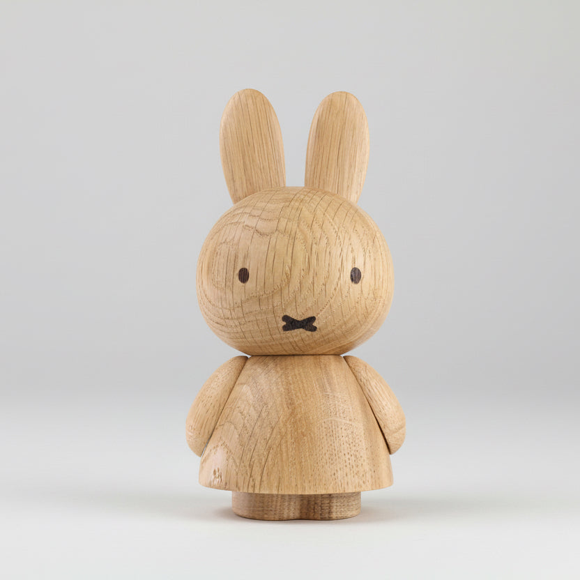 Wooden figurine of an animated cartoon character carved from light oak, featuring long upright ears, simple dot eyes and crossed mouth detail, a rounded sculpted body with small arms, visible natural wood grain, and a matte surface on a plain white background.