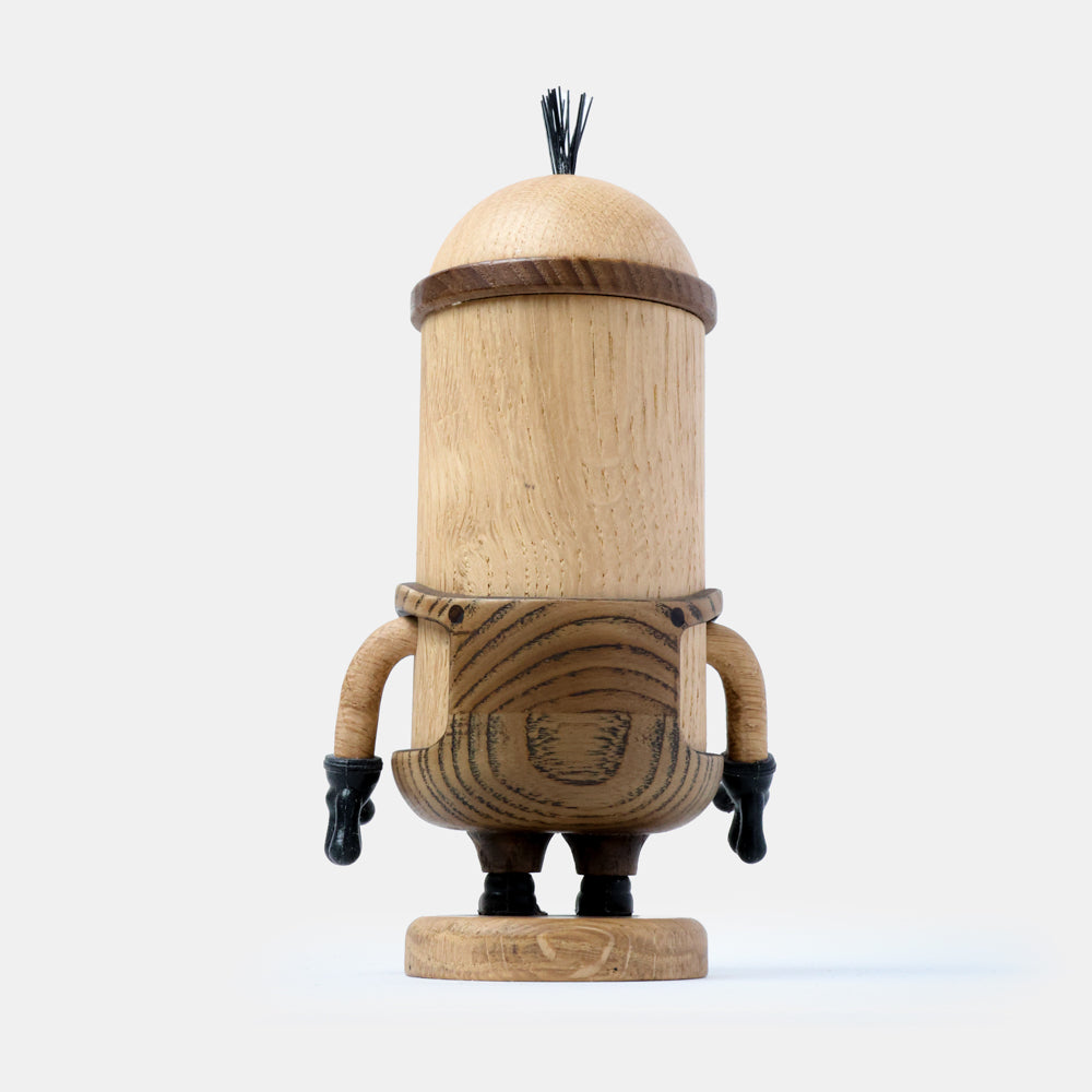 Back view of a wooden figurine of an animated cartoon character carved from light and dark wood, featuring a tall cylindrical body, rounded head with small hair detail, sculpted arms with dark gloves, short legs, visible natural wood grain, and a matte surface on a plain white background.