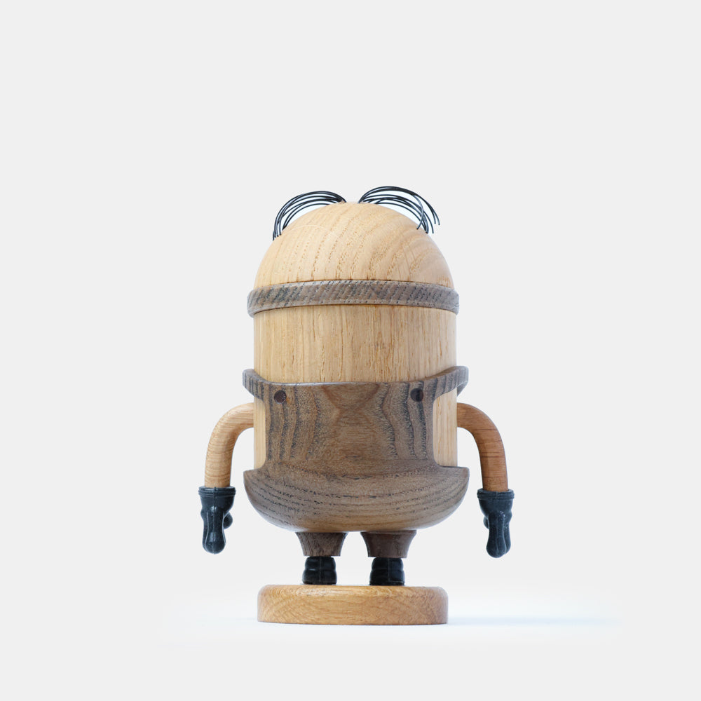 Back view of a wooden figurine of an animated cartoon character carved from light and dark wood, featuring a rounded cylindrical body, engraved clothing details, small sculpted arms with dark gloves, short legs, visible natural wood grain, and a matte surface on a plain white background.