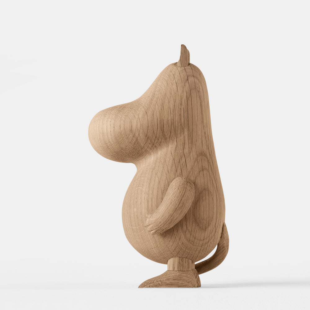 Wooden figurine of an animated cartoon character carved from light oak, featuring a rounded elongated head with small ear details, a smooth sculpted body, simplified limbs, visible natural wood grain, and a matte surface on a plain white background