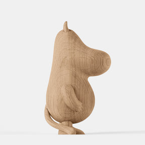 Wooden figurine of an animated cartoon character carved from light oak, featuring an elongated rounded head with small ear detail, a smooth sculpted body, simplified limbs and tail, visible natural wood grain, and a matte surface on a plain white background.