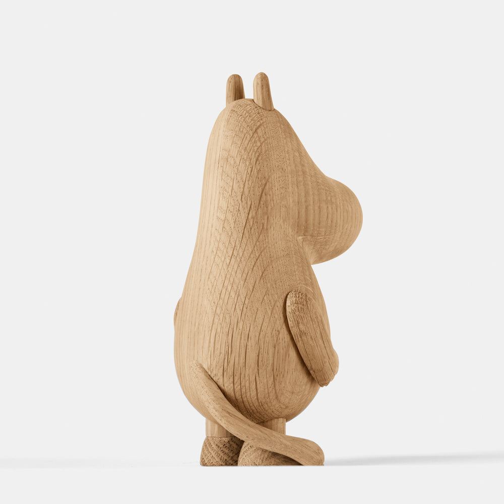 Wooden figurine of an animated cartoon character carved from light oak, featuring an elongated rounded head with small ear details, a smooth sculpted body, simplified limbs and tail, visible natural wood grain, and a matte surface on a plain white background.