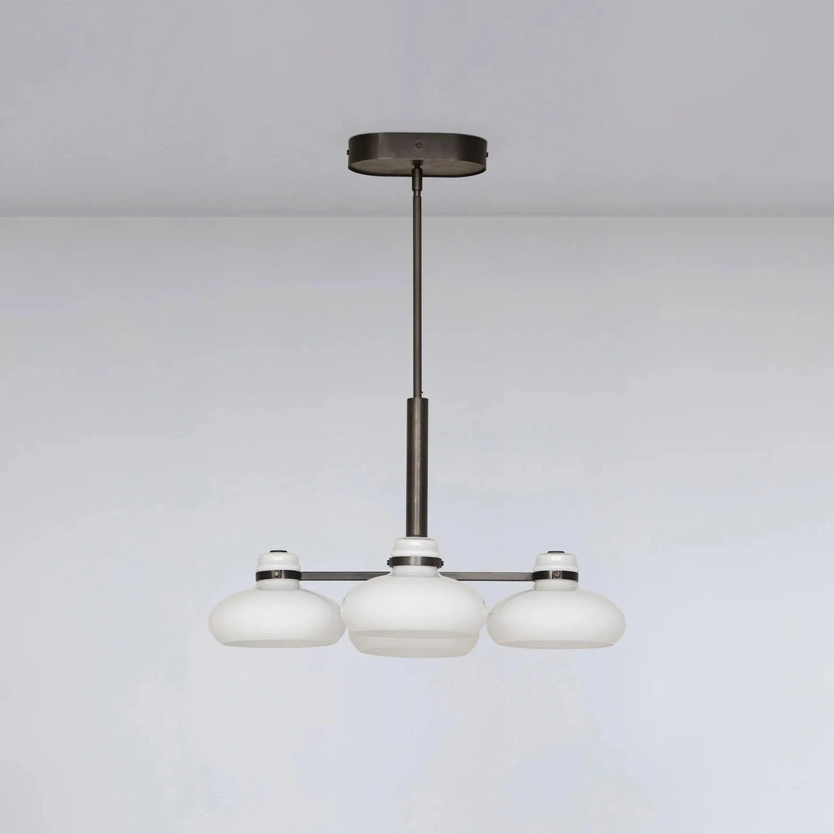 Modern chandelier with three white glass shades on a plain background