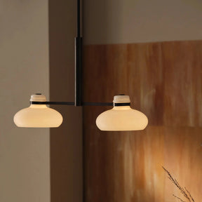 Modern pendant light fixture with two round shades in a room with wooden wall and plant.