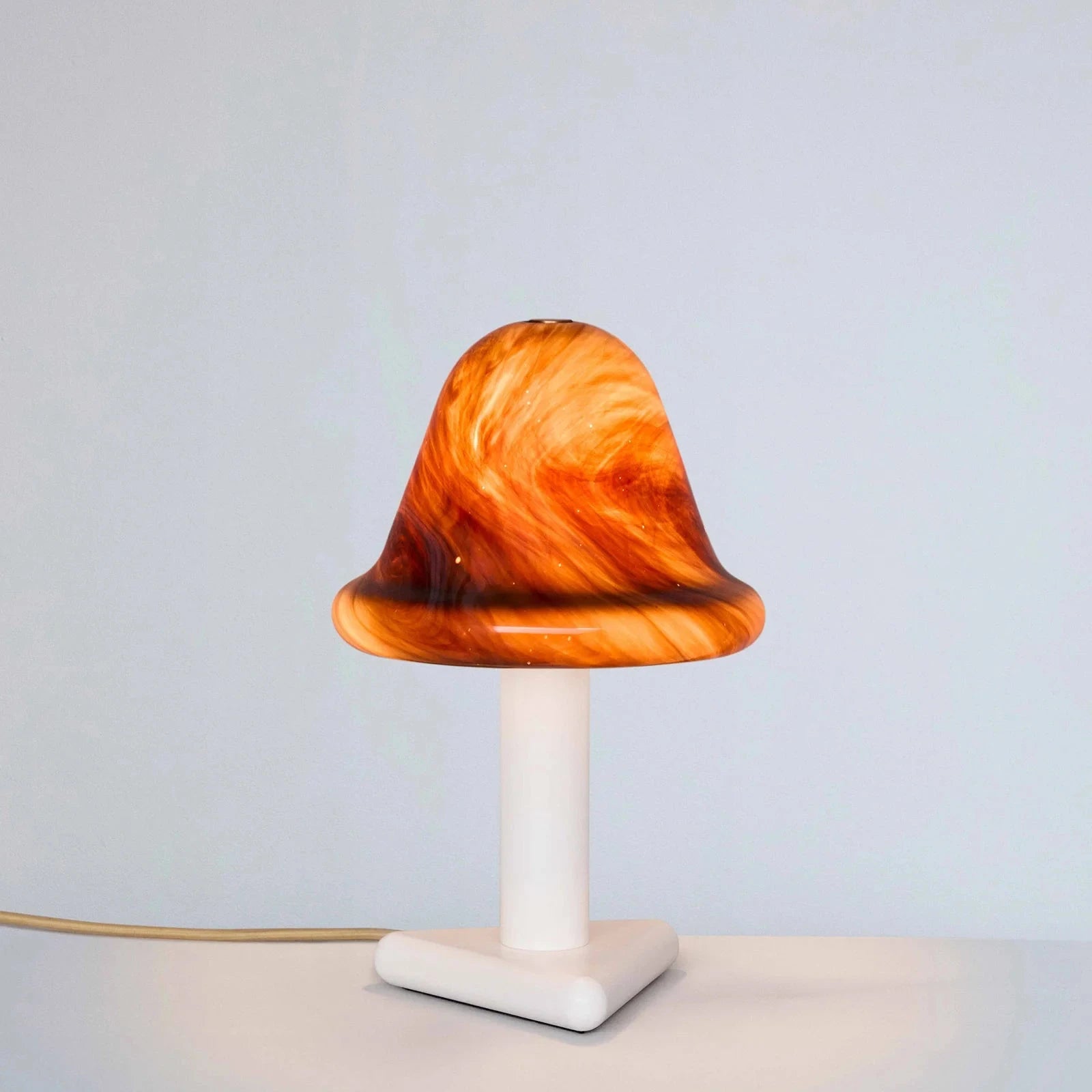 Mushroom-shaped lamp with orange and brown marbled design on a white base against a light gray background