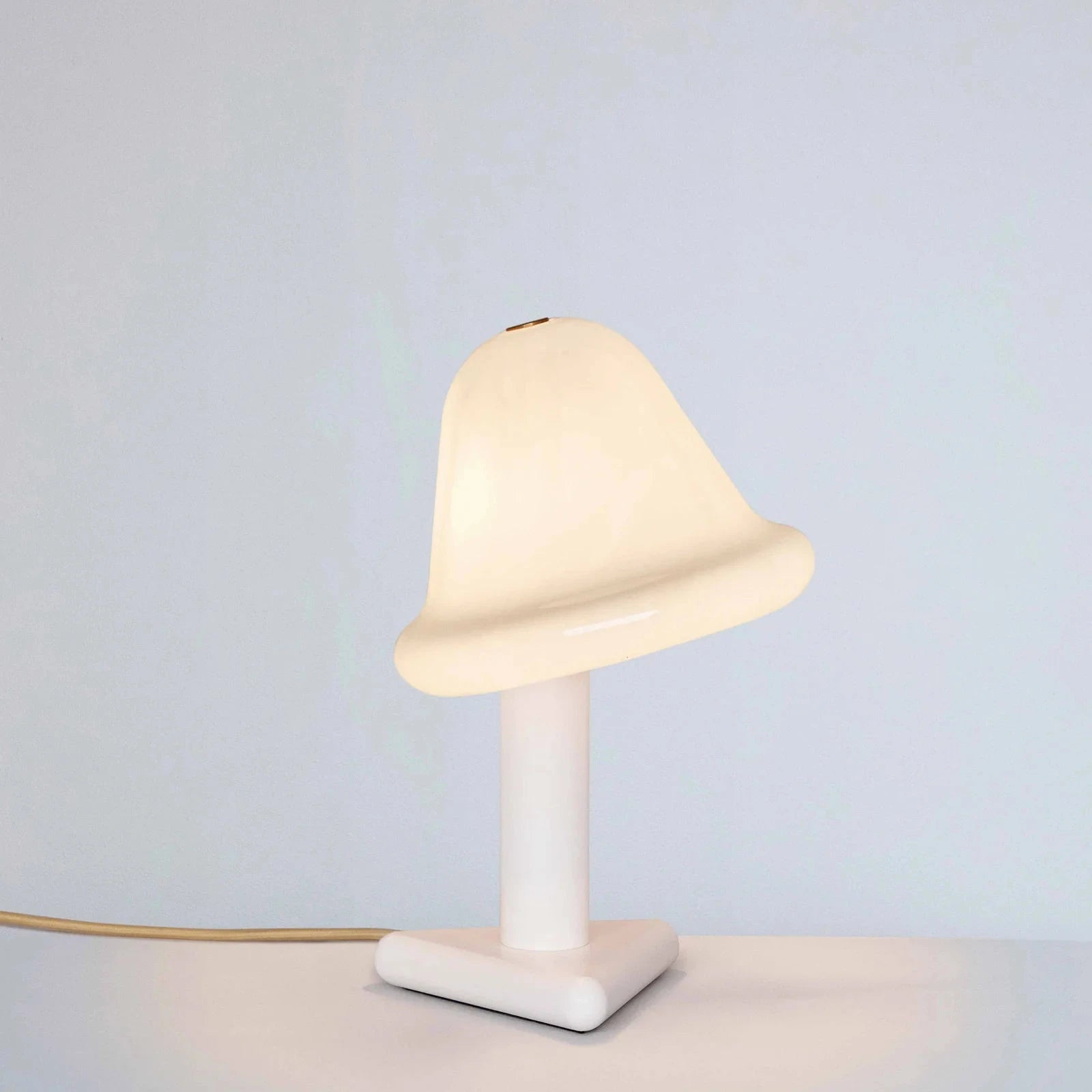 Small table lamp with a white base and bell-shaped glass shade on a light gray background